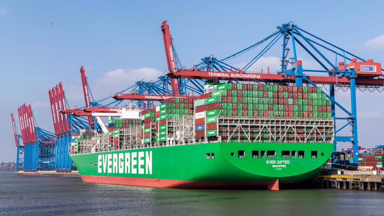 Evergreen cargo ship docked at Hamburg Harbor with cranes and blue sky.
